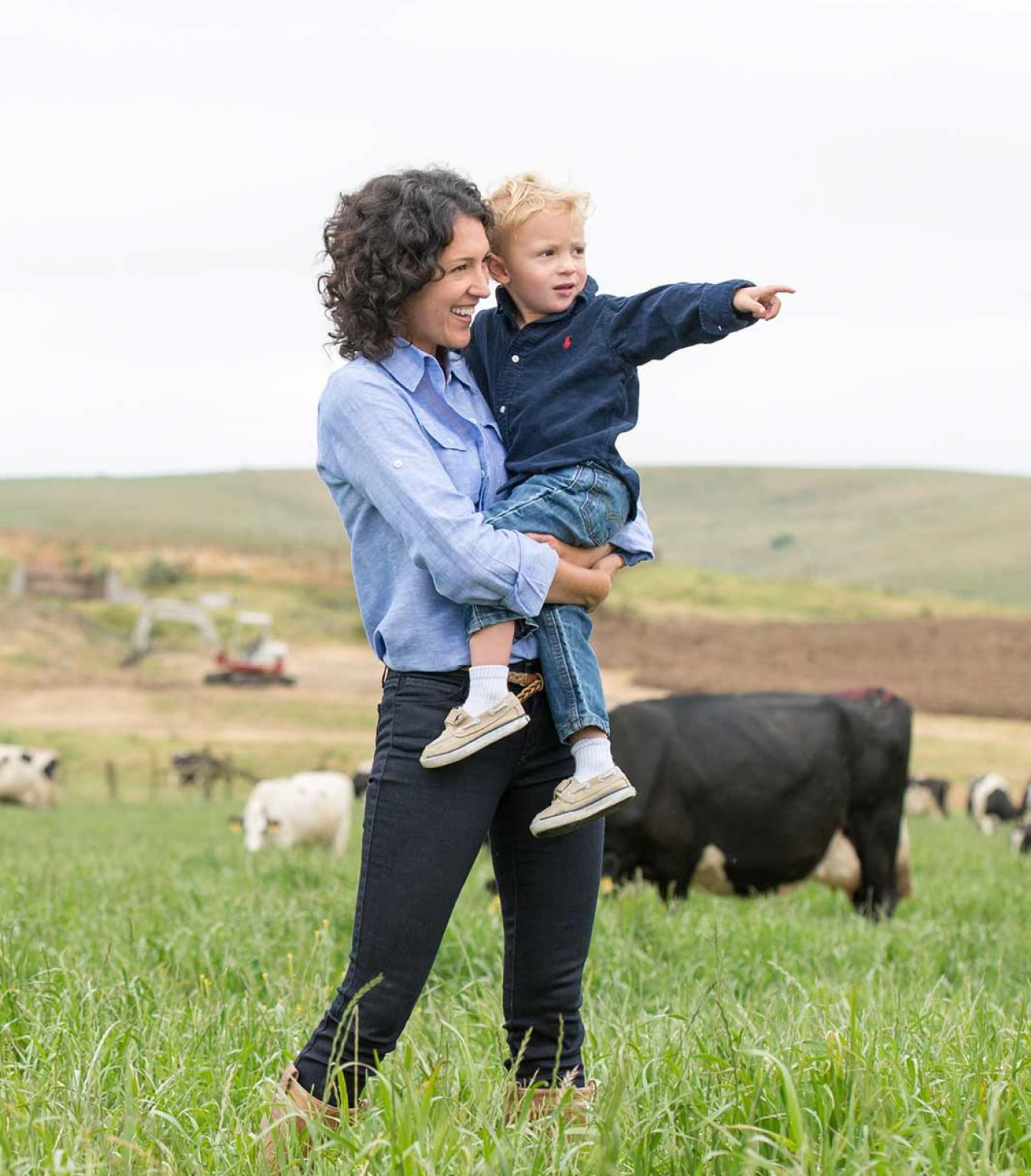 Mother holding son on a farm surrounded by cows